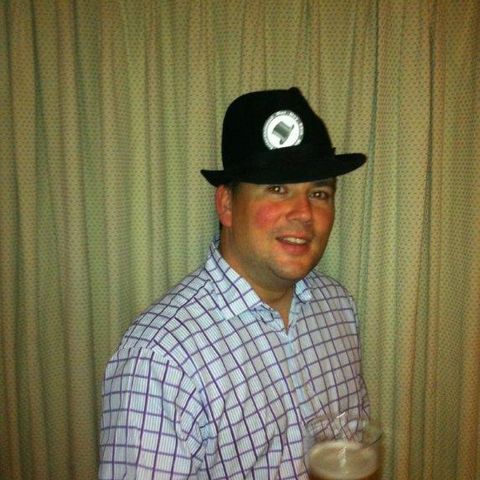A man in a black bowler hat raising a pint