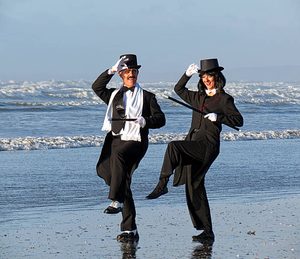 Two dancers in top hats and tails high-stepping on a beach