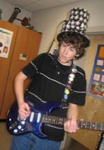A student playing electric guitar in a tall novelty top hat