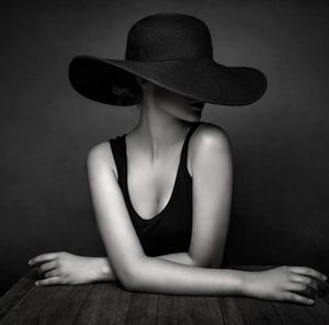 A black-and-white portrait of a woman in a wide-brimmed black hat
